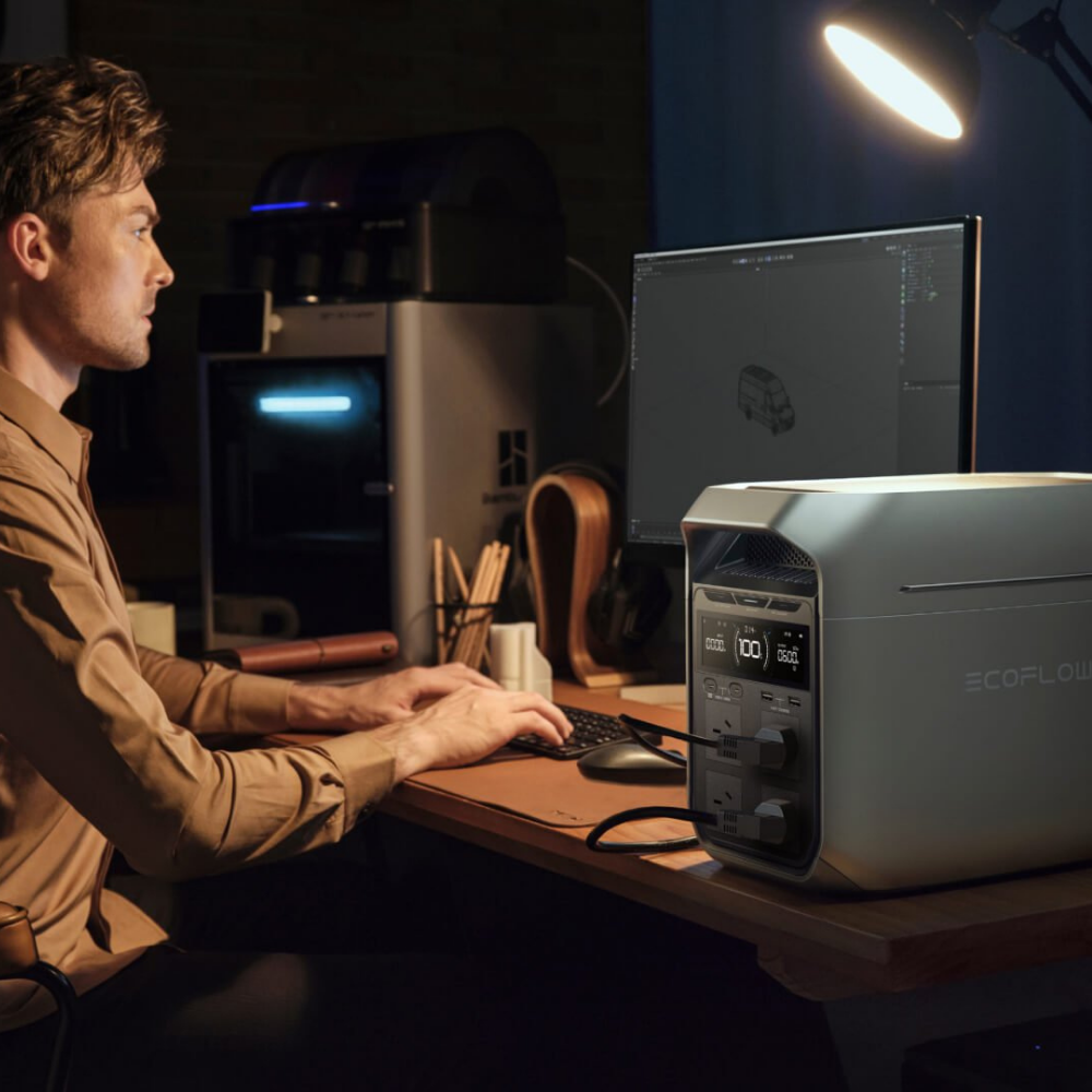 Person working at a desk with a computer and EcoFlow device in a dimly lit room.