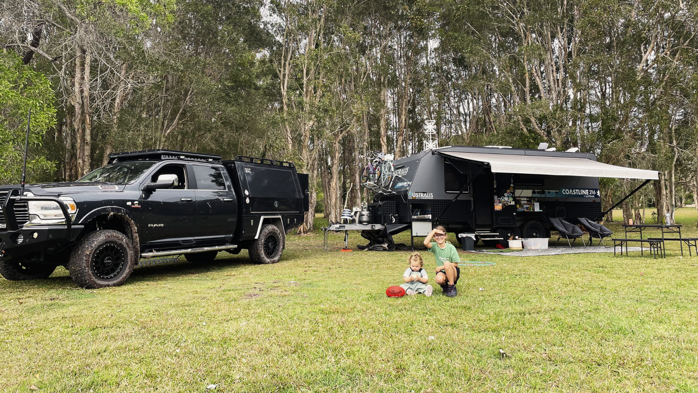 Black truck and camper trailer on grass with trees in the background