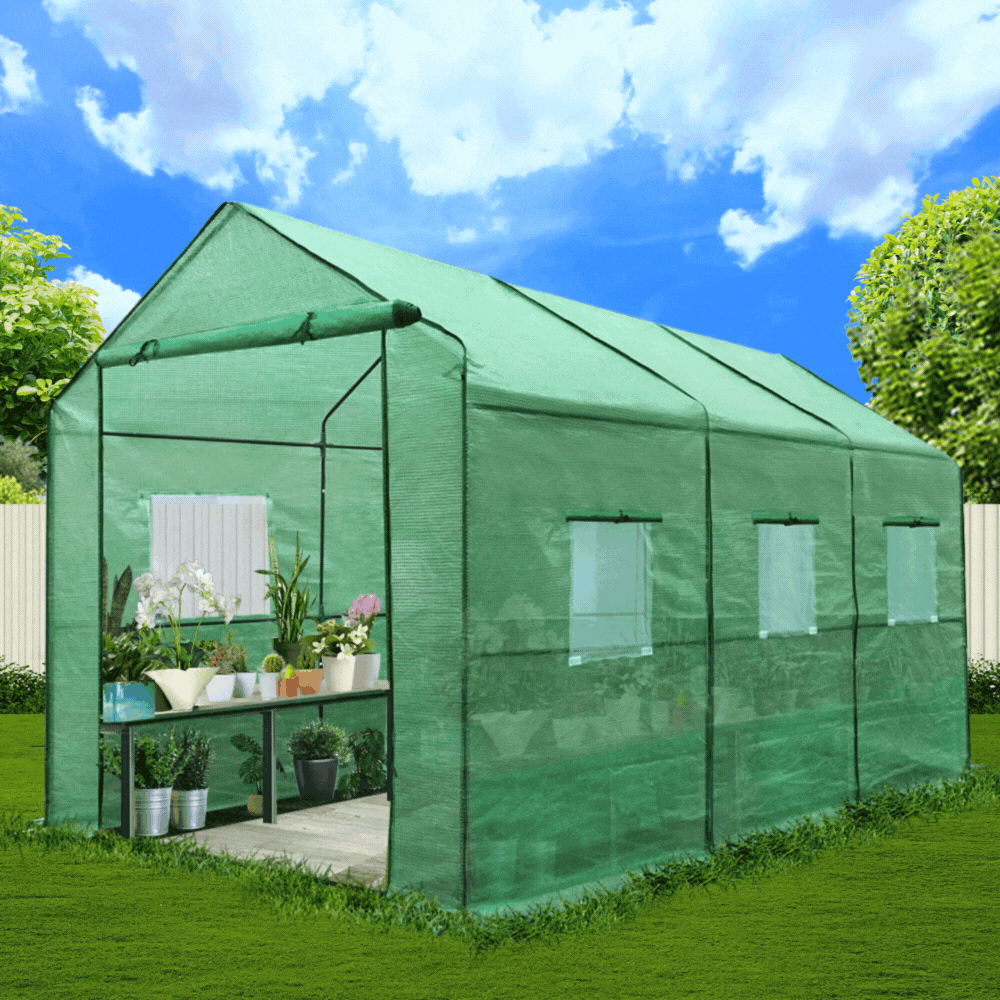 A small, walk-in greenhouse with a green, mesh fabric cover and an open zipped door is set on a lawn with various potted plants inside.