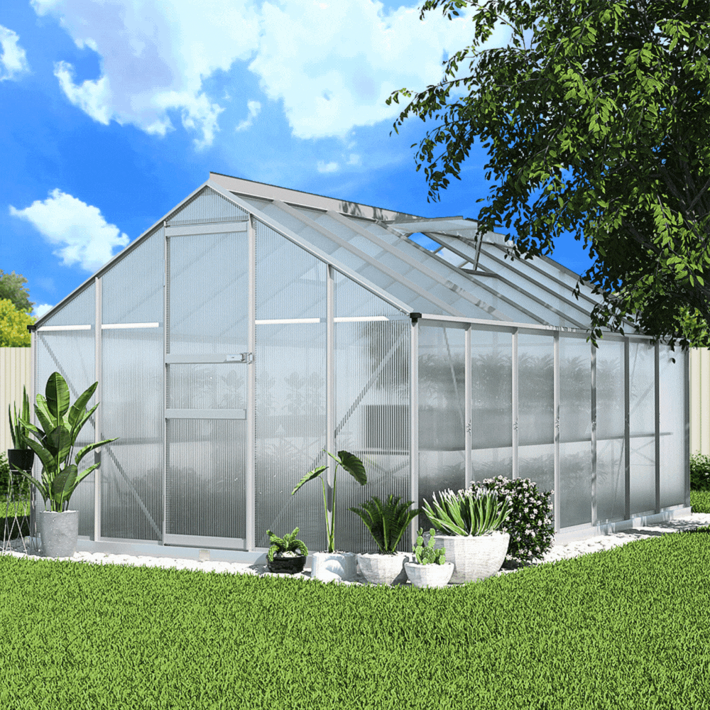 A polycarbonate greenhouse shed with an open door and roof vent, surrounded by various potted plants in a sunny garden.