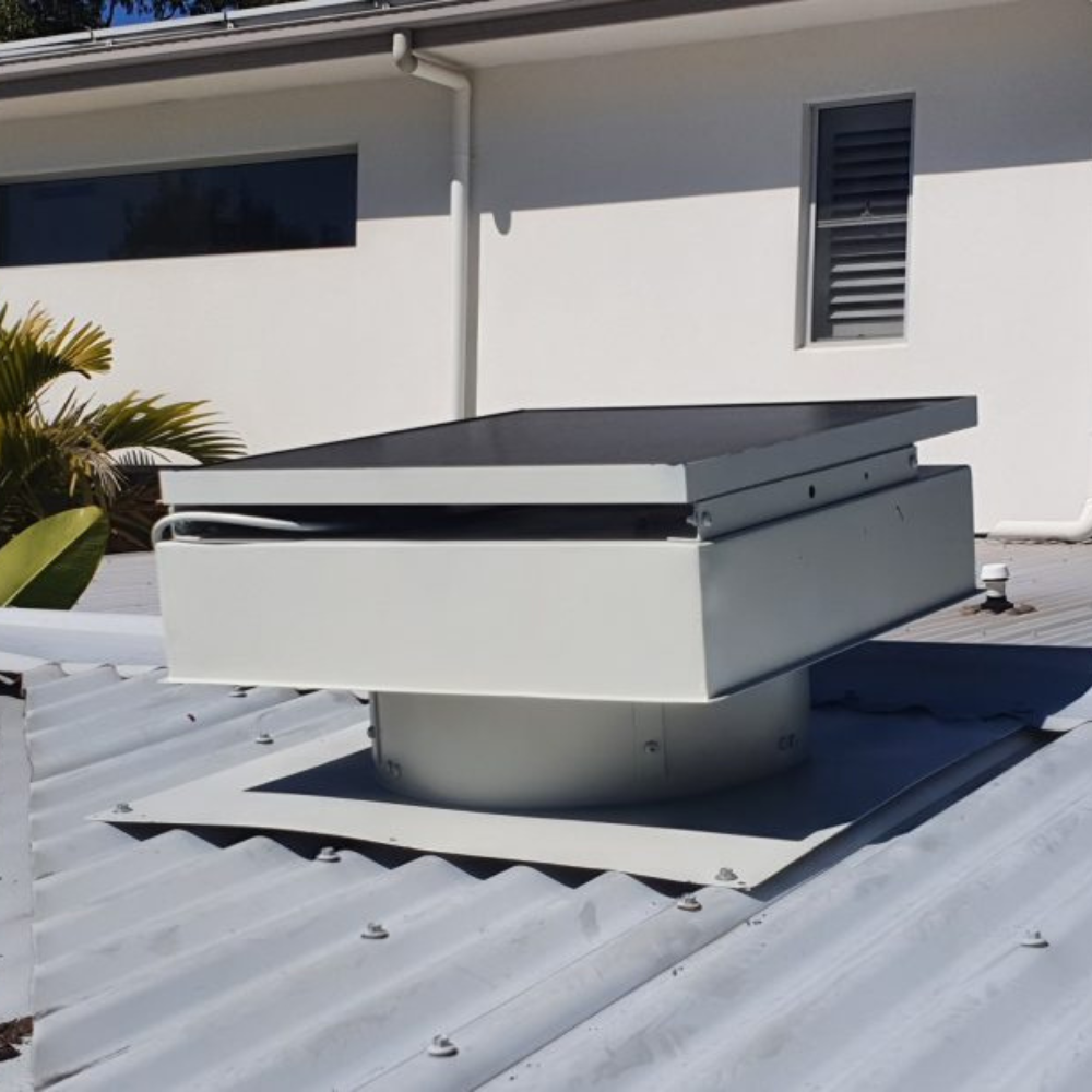 Beige ventilator with a flat panel on a grey corrugated roof beneath a white eave.