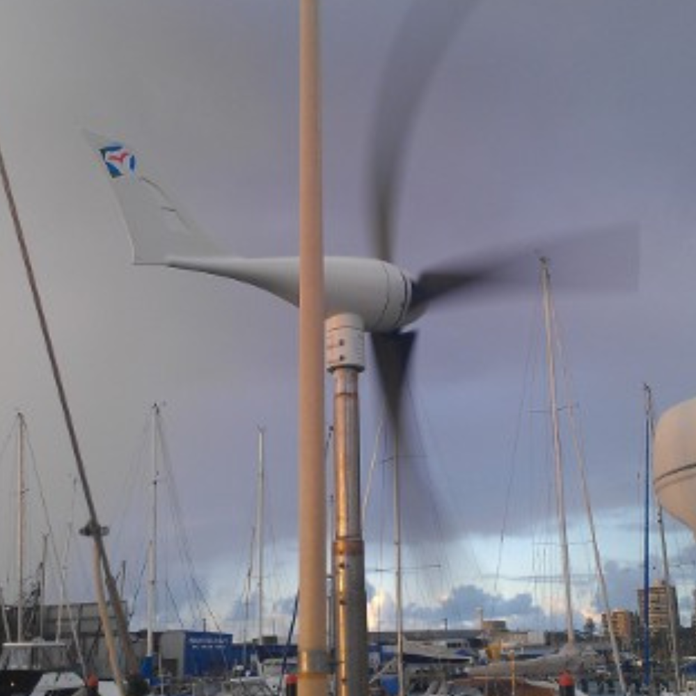 Wind turbine in motion at a marina, with blurred blades indicating rotation and boats in the background.
