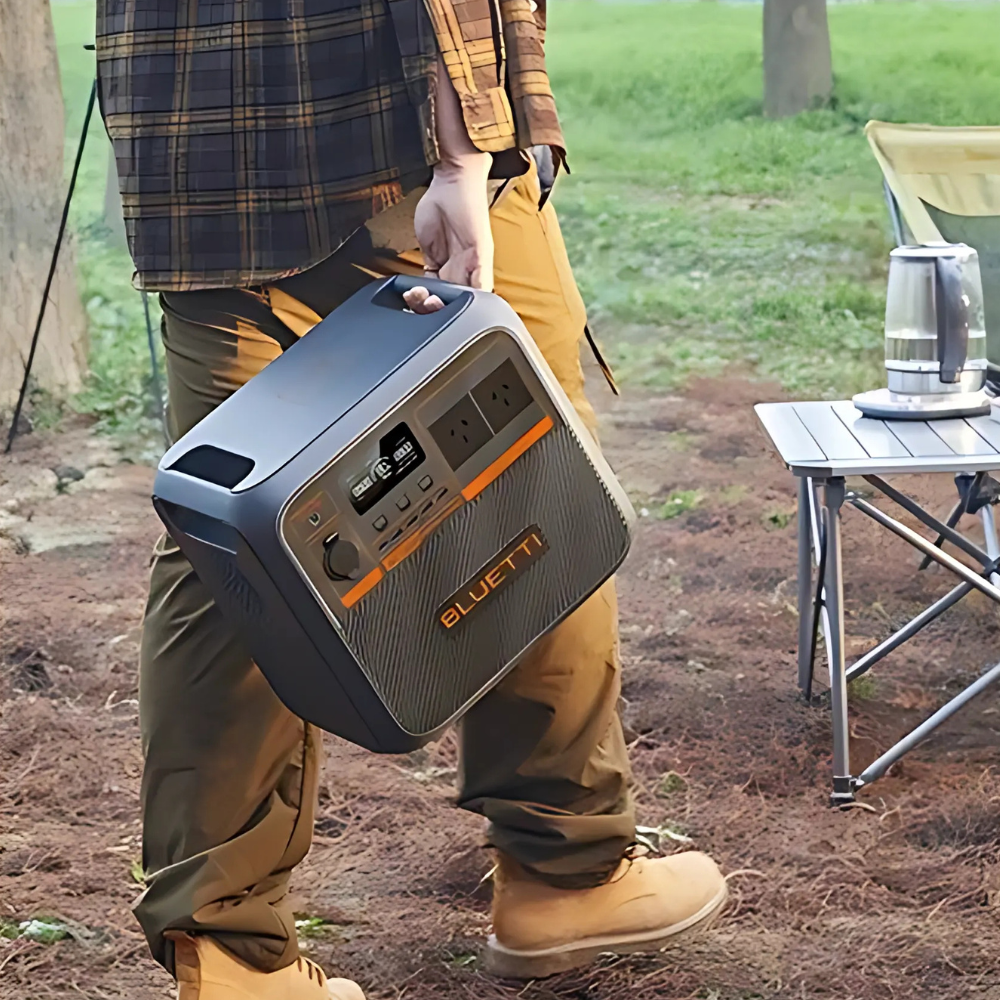 Person carrying Bluetti unit by its built-in handle, walking toward a campsite setup, demonstrating portable convenience.