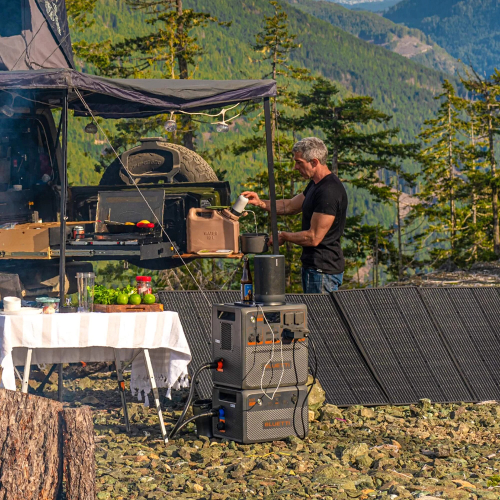 Outdoor camping scene with Bluetti power station and solar panels, used by a camper in a forest setting with canopy and gear.