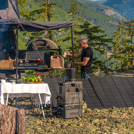 Outdoor camping scene with Bluetti power station and solar panels, used by a camper in a forest setting with canopy and gear.