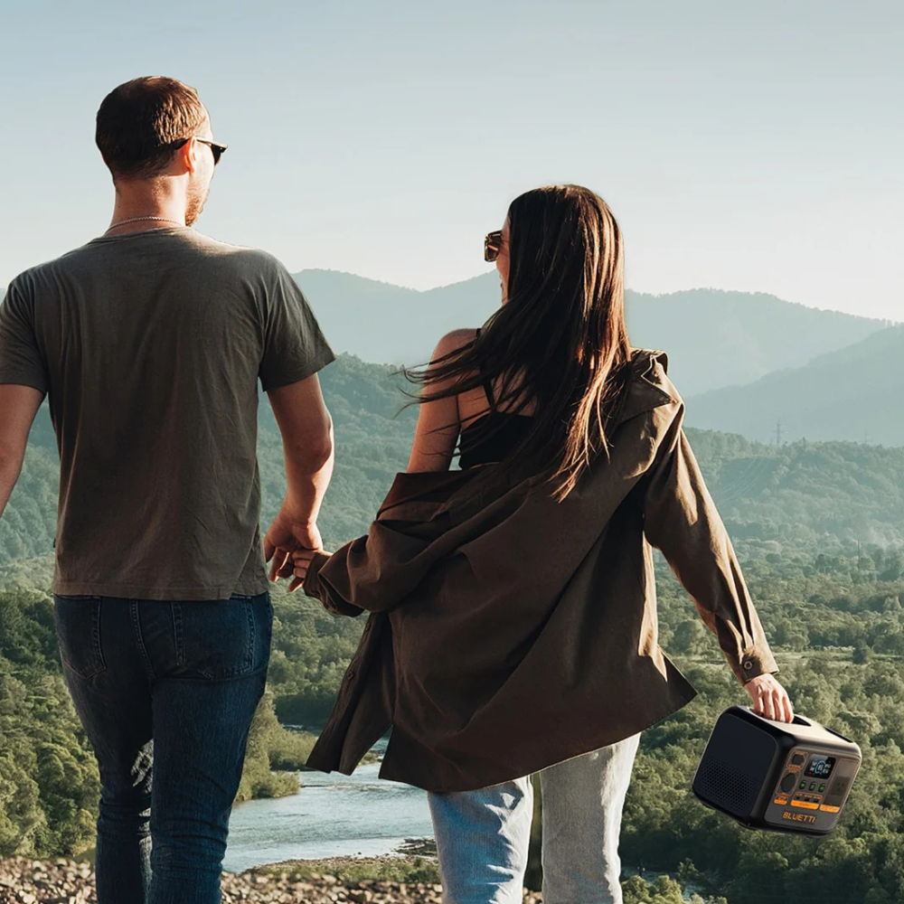 Couple walking outdoors carrying Bluetti power station together.