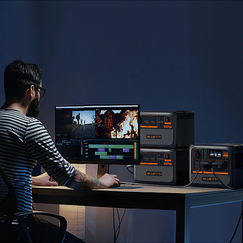 Man using Bluetti power station at night to power a computer workstation, showcasing indoor use and screen lighting.