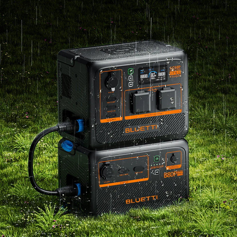 Bluetti unit stacked with another power module outdoors in a grassy forest setting, indicating extended battery configuration for off-grid use.