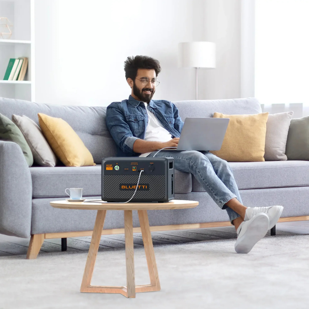 Man relaxing on a couch with Bluetti unit powering a laptop, demonstrating quiet and efficient indoor usage.