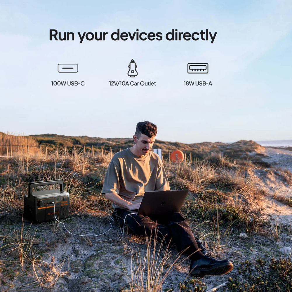 Person using Bluetti unit while sitting on rocky terrain, highlighting direct device charging outdoors.