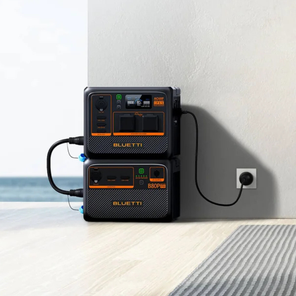 Bluetti unit charging via wall outlet, shown plugged in and upright against white tiles.