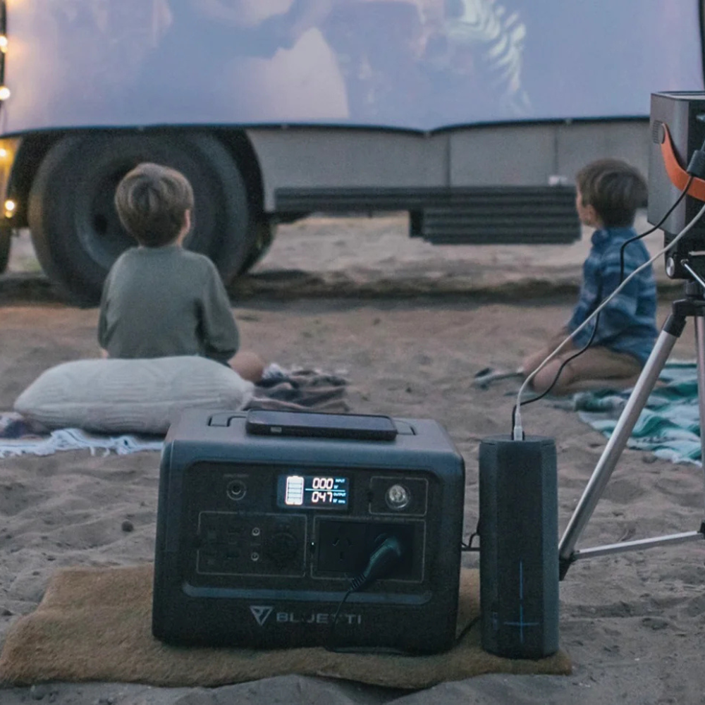 Two people camping with a Bluetti unit in front of a van.