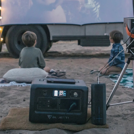 Two people camping with a Bluetti unit in front of a van.