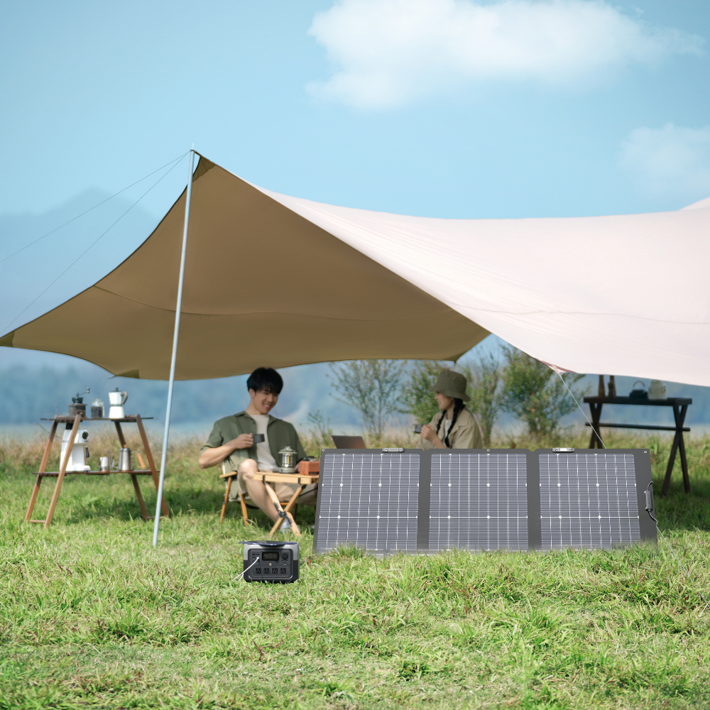 Two people sitting under a large beige tent with a solar panel on a grassy field.