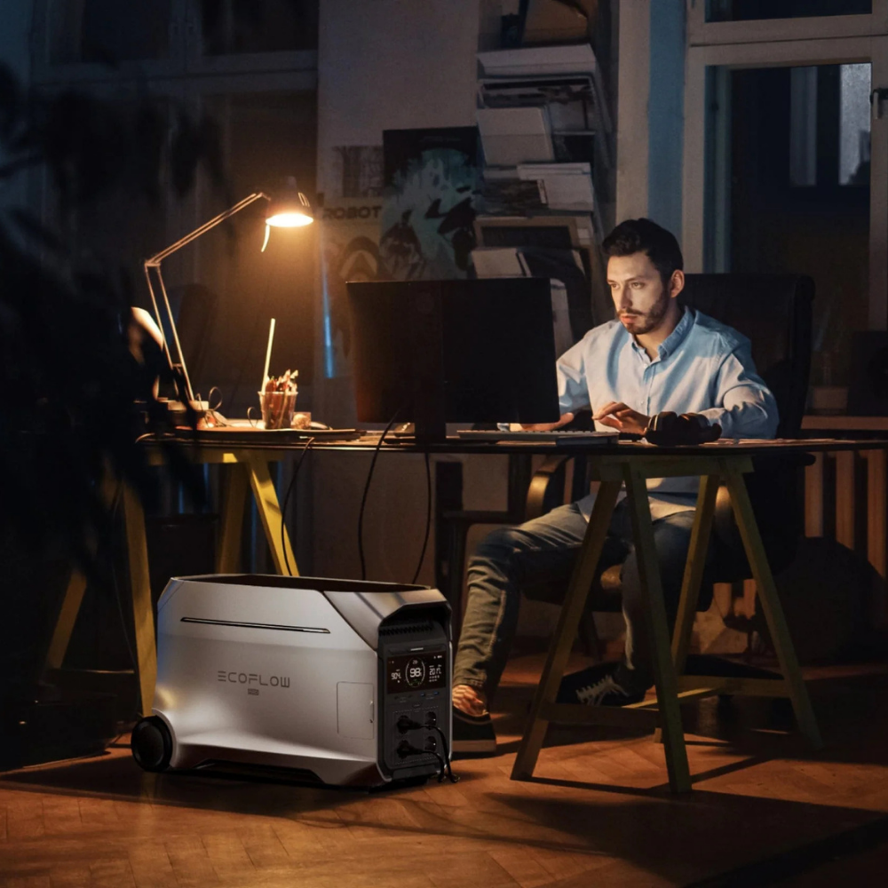 Man working on a laptop at a desk with a portable power station in front of him.