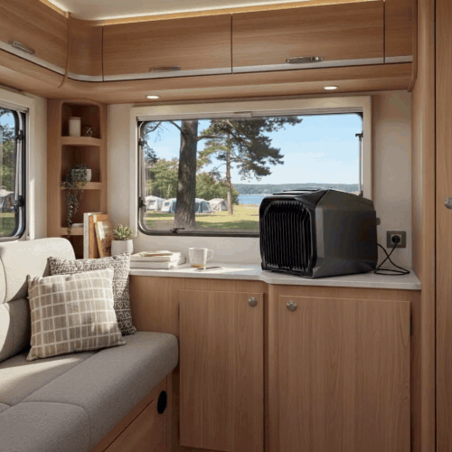 Interior of a camper with wooden cabinets, a window view of trees, and a black air conditioner.