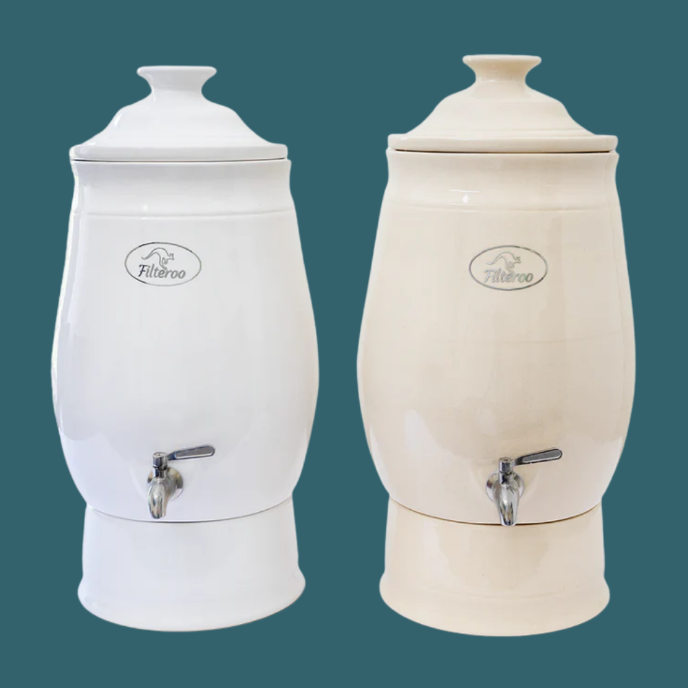 Two white ceramic water dispensers with silver faucets on a teal background