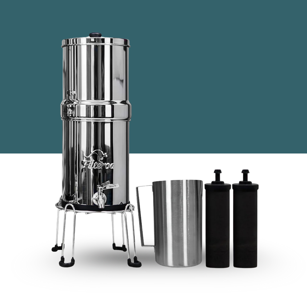 Stainless steel gravity water filter system with stand, two black filter cartridges, and a metal jug shown against a split dark teal and grey background.