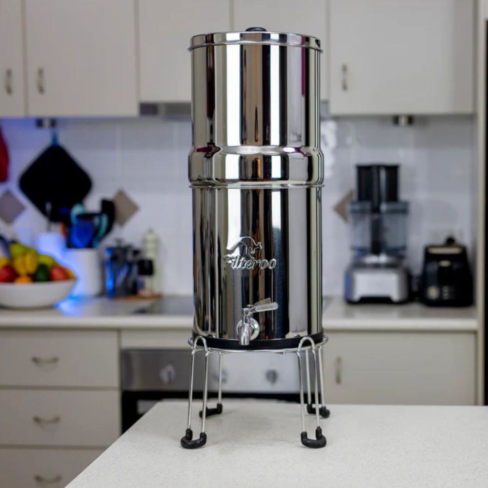 Gravity water filter in kitchen setting, placed on a benchtop near a sink, demonstrating everyday home use.