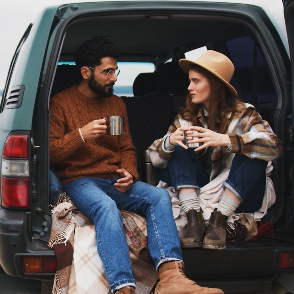 Couple drinking from cups while sitting at the back of a vehicle with a Filteroo unit beside them, illustrating off-grid use.