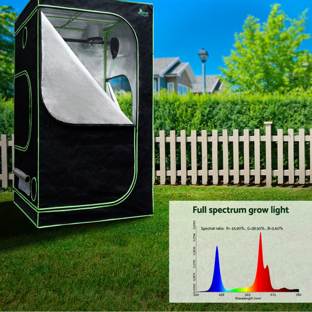 Black grow tent with a full spectrum light chart on grass, house, and trees in the background