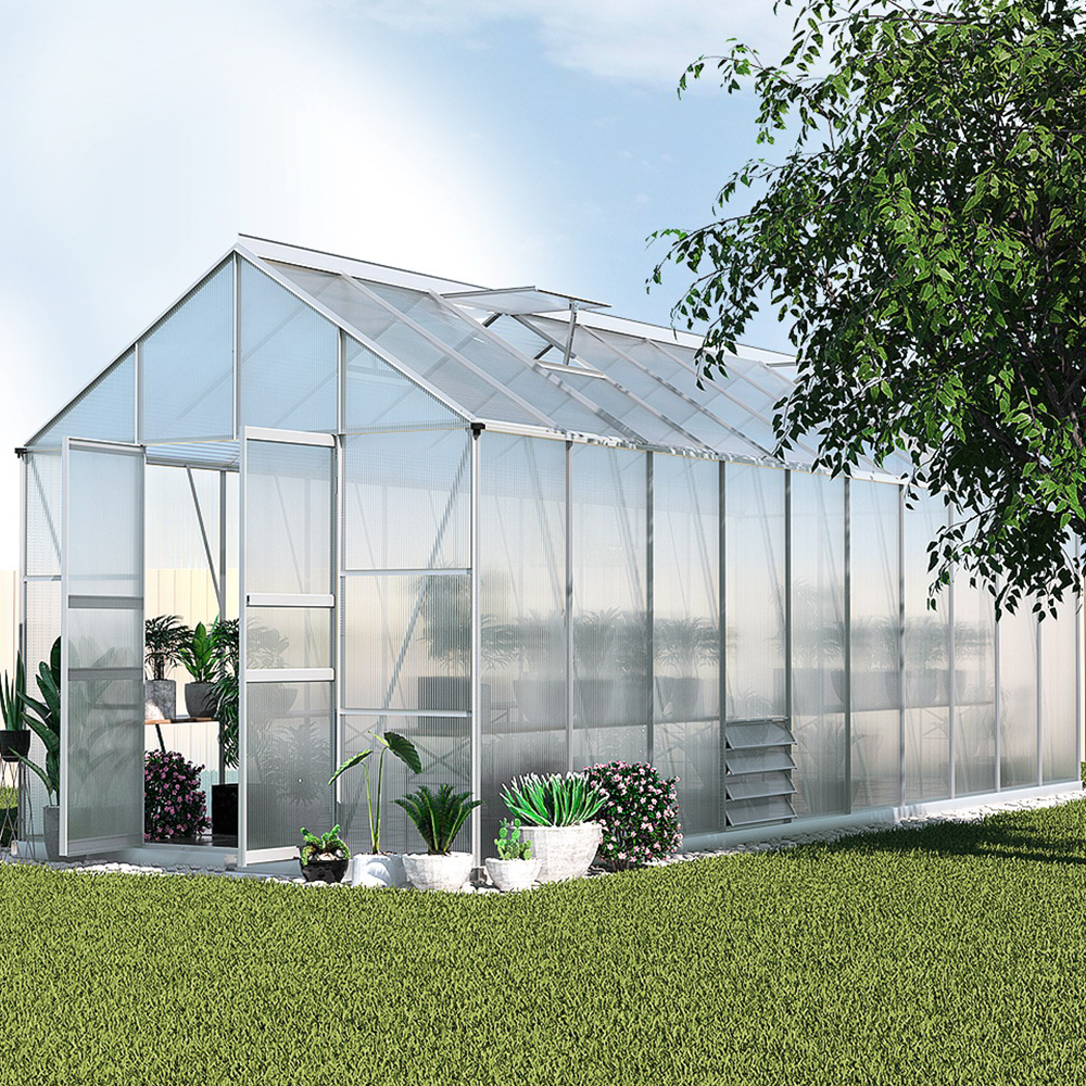 The greenhouse placed outdoors in a garden setting, surrounded by plants and greenery, showcasing the spacious interior and transparent walls