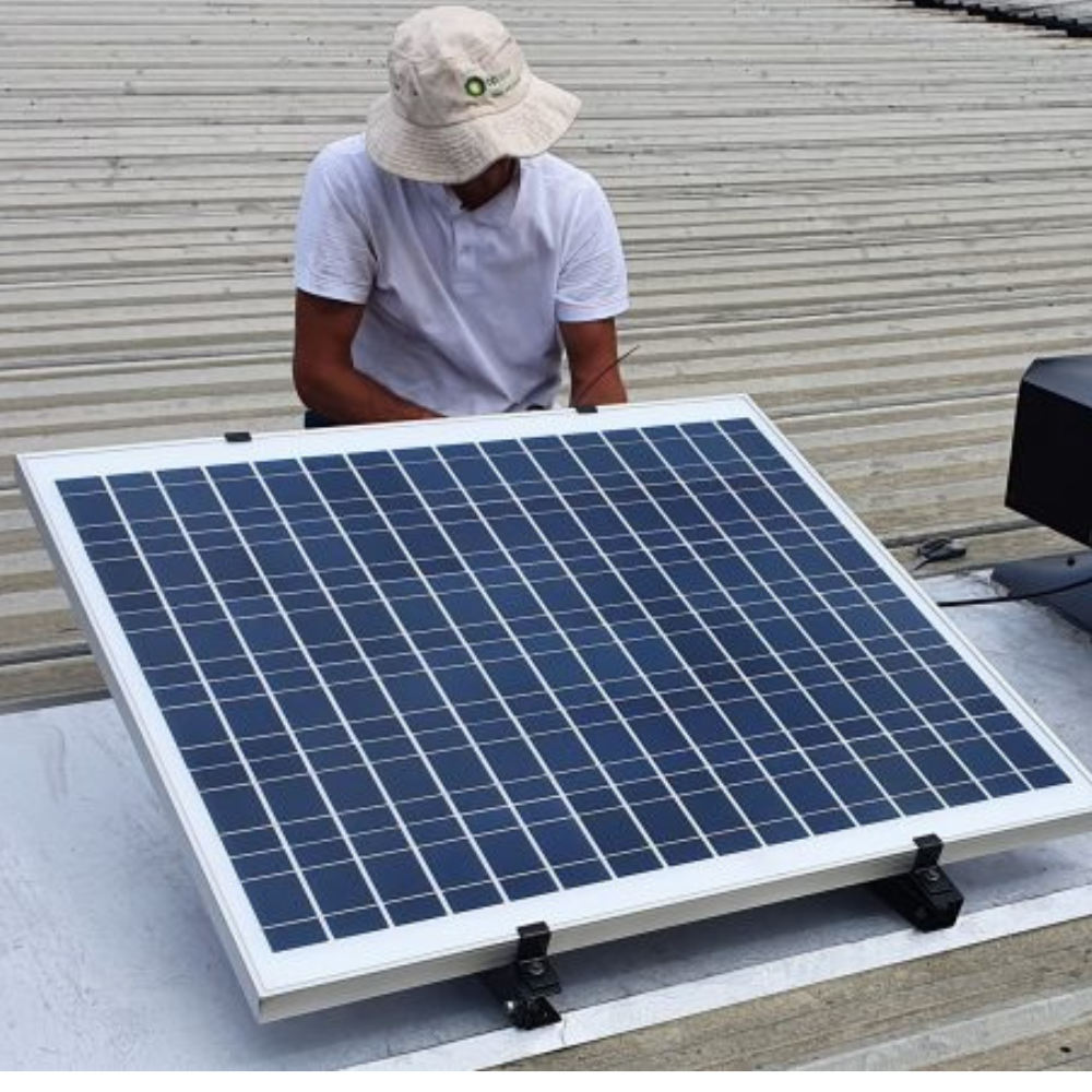 Technician in a hat installing a solar panel on a corrugated metal roof.