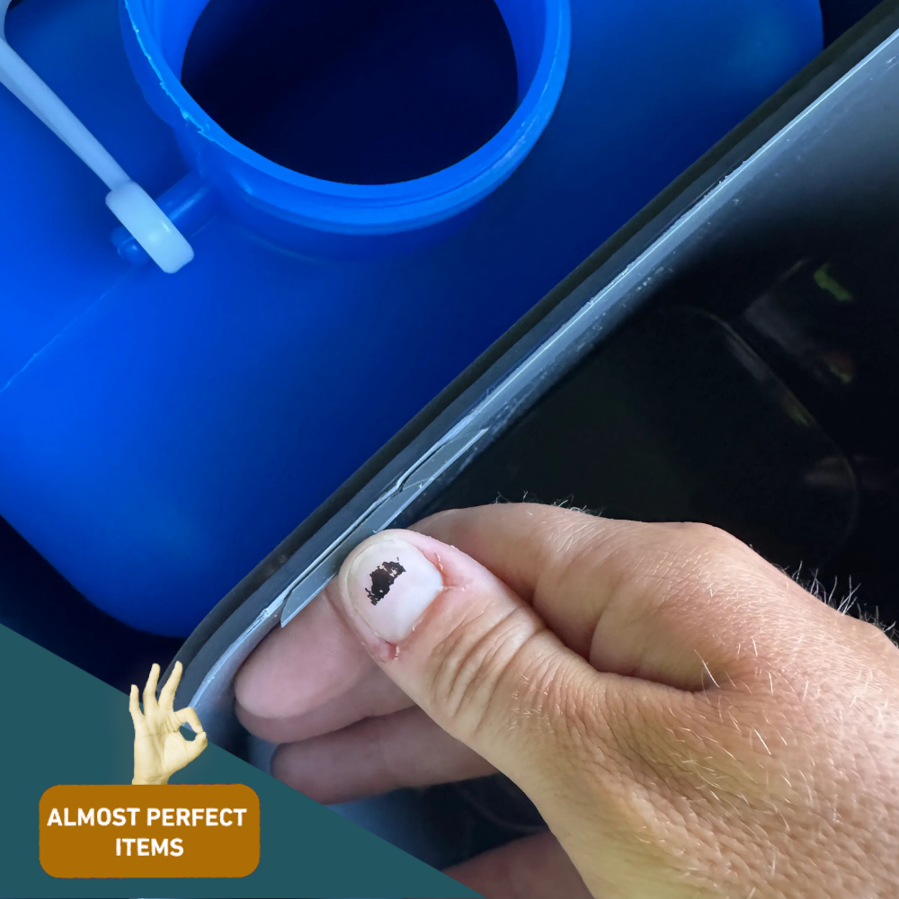 Image of inner rim with blue tank (hand holding edge):
Close-up of a minor flaw on the inner plastic rim of a Trelino composting toilet above a blue waste tank, with hand inspecting the edge.