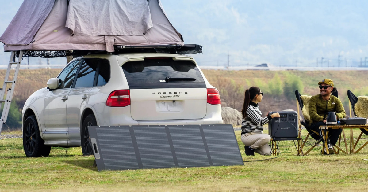 Alt text: Couple camping with a Porsche Cayenne SUV, rooftop tent, portable solar panels, and a Bluetti power station on grassy field.