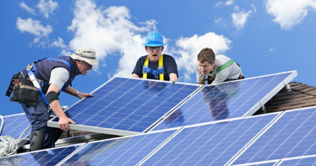 Three workers on a roof installing solar panels. One worker in the middle looks up with a frustrated expression, mouth agape.