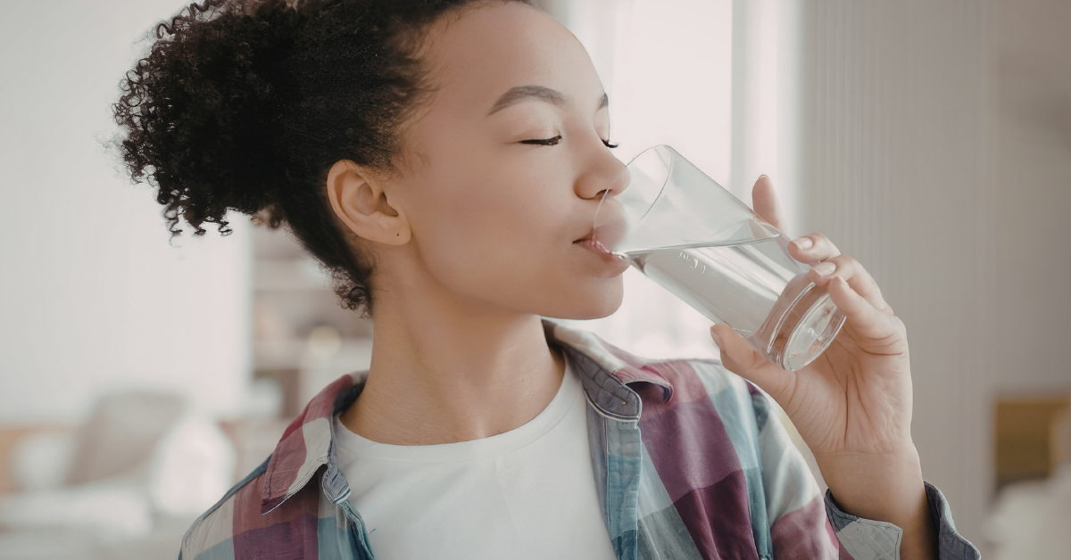 a woman with curly hair drinks clear water from a glass.