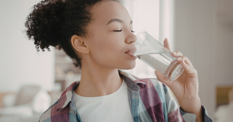 a woman with curly hair drinks clear water from a glass.
