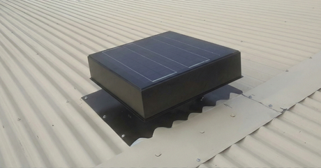 A square, black solar-powered ventilator mounted on a corrugated metal roof.