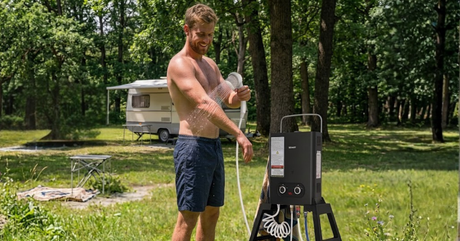 A person using a portable water heater at a campsite with a scenic outdoor backdrop.