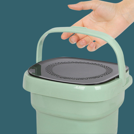 Person lifting the green portable washing machine using the built-in handle.


