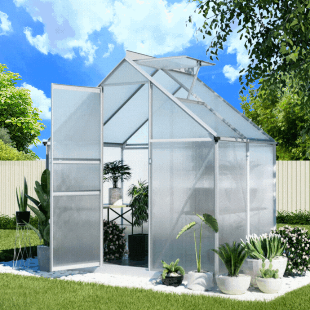 A small, walk-in greenhouse with an open  door is set on a lawn with various potted plants inside.