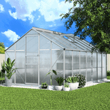 A polycarbonate greenhouse shed with an open door and roof vent, surrounded by various potted plants in a sunny garden.
