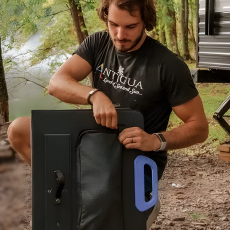 A man at a camping site unfolds the BLUETTI solar panel. The lush green forest and a camper in the background highlight the product's portability for outdoor enthusiasts