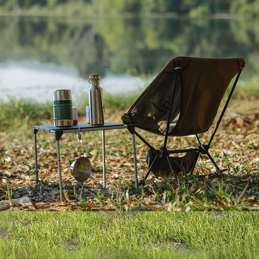 
Outdoor camping setup by a serene lakeside with a brown folding chair and a small table holding a thermos, water bottle, and camping gear