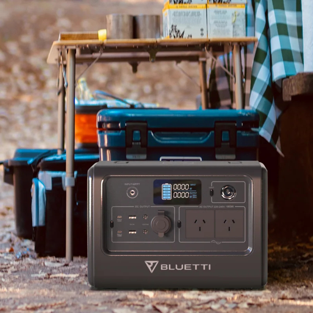 Bluetti AC70 power station placed on a wooden table beside camping equipment.

