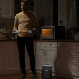 Man holding a plate of food in a kitchen with a dehumidifier on the floor.