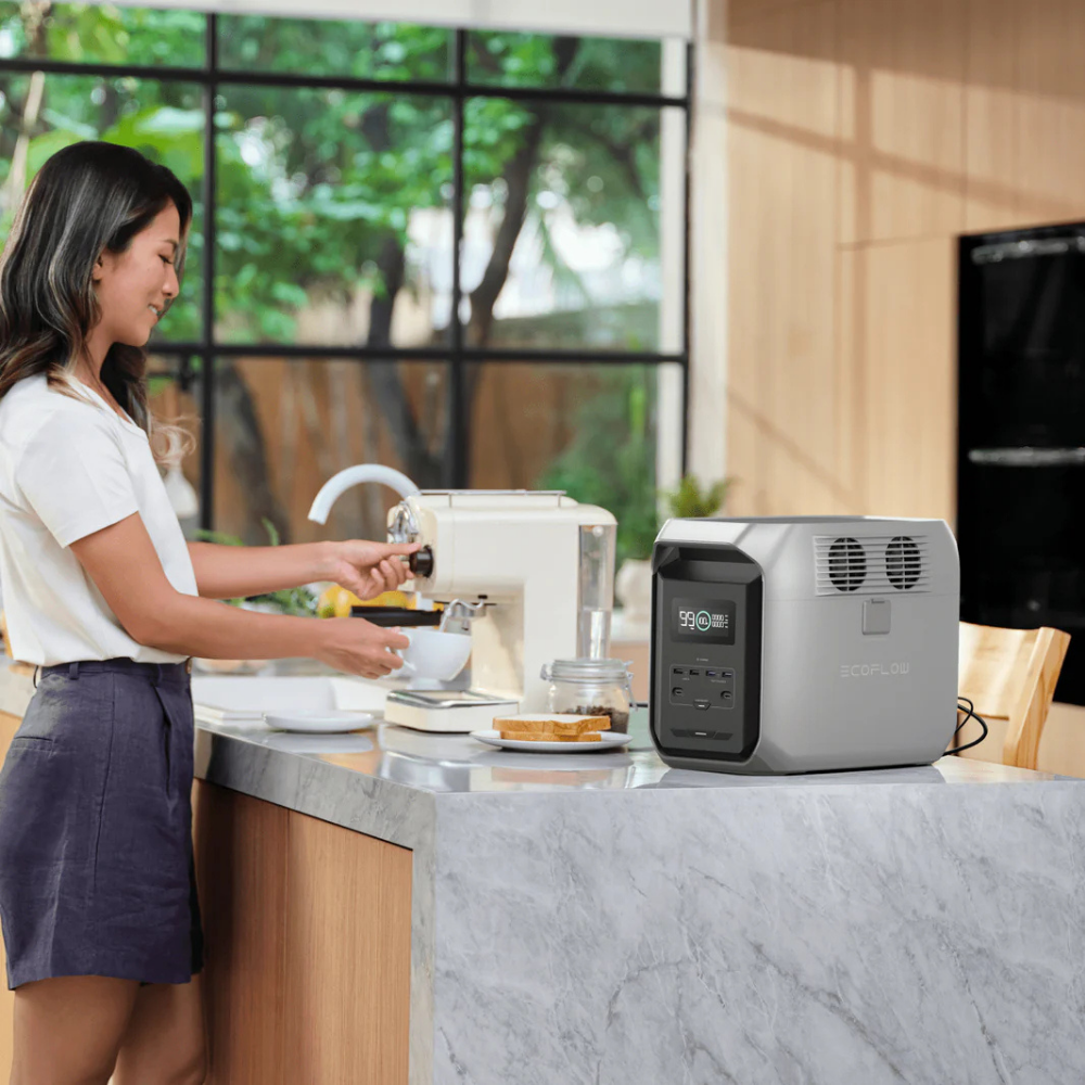 Woman using a coffee machine on a kitchen counter with a portable power station nearby.