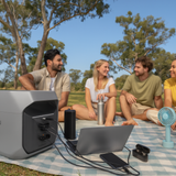 Group of people sitting on a blanket outdoors with electronic devices
