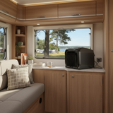 Interior of a camper with wooden cabinets, a window view of trees, and a black air conditioner.