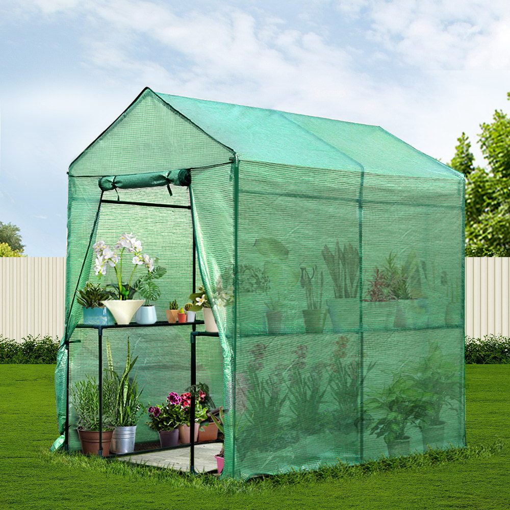 Green portable greenhouse with plants inside on a grassy area