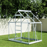 Metal greenhouse structure on grass with trees in the background