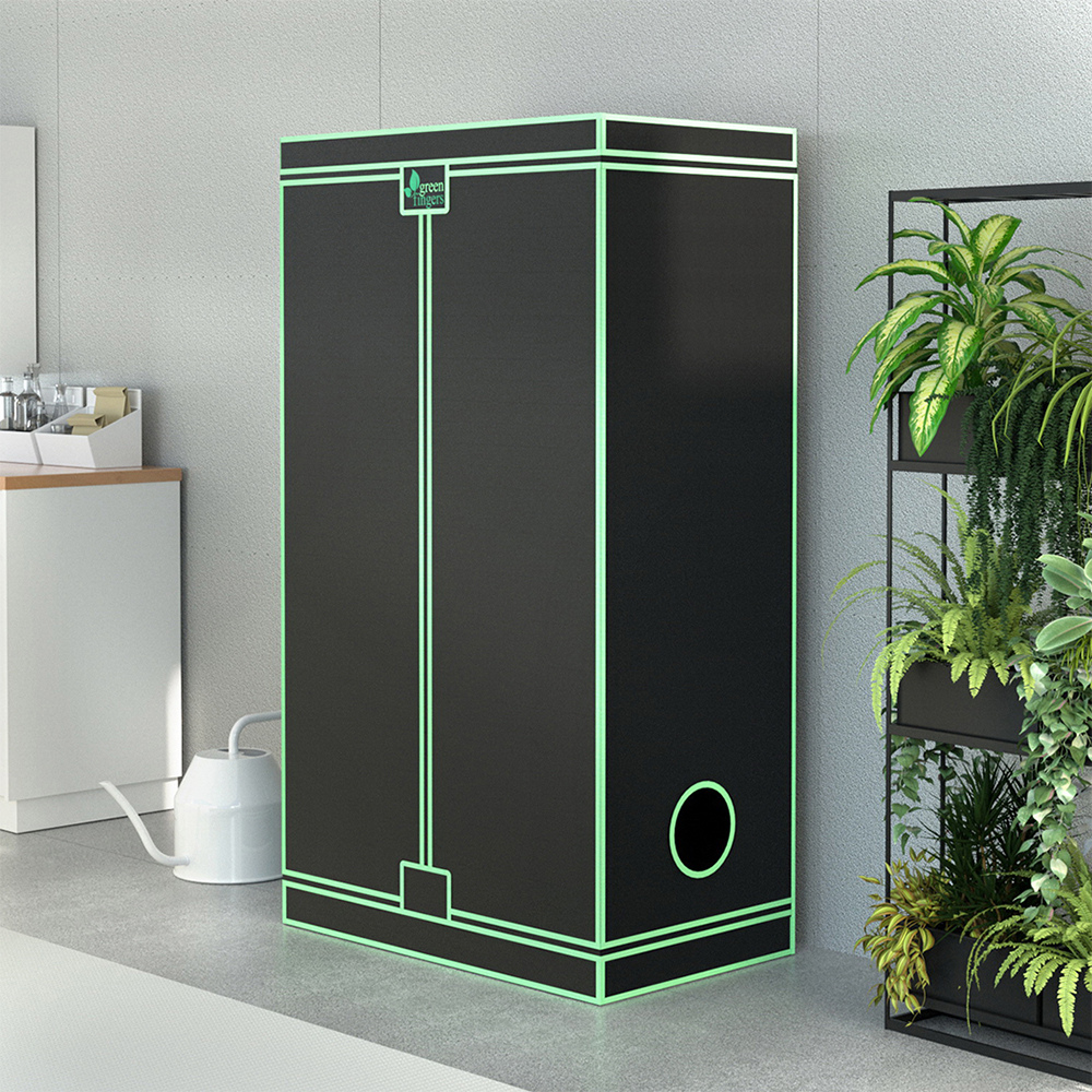 Black grow tent with green accents in a room with plants and a watering can.