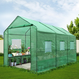 Green greenhouse with plants inside on a grassy area with trees in the background