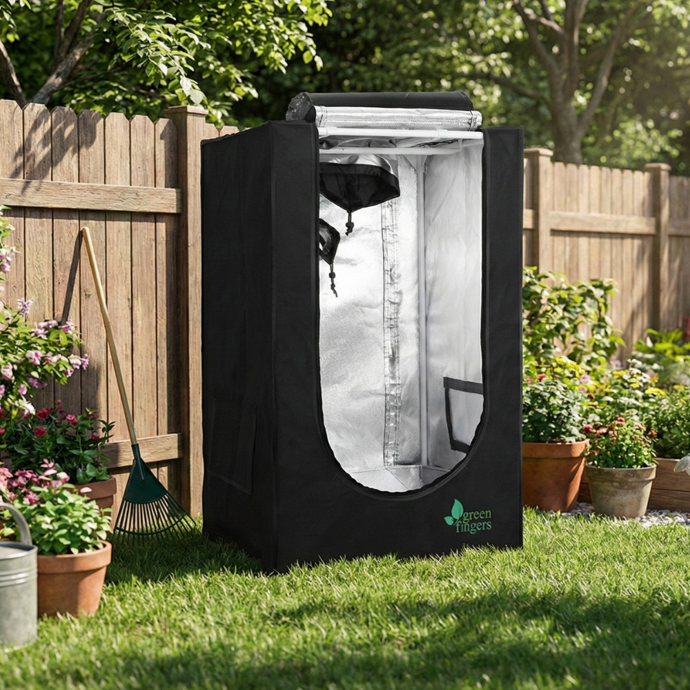 Black grow tent with transparent door on a grassy area with plants and a wooden fence in the background.