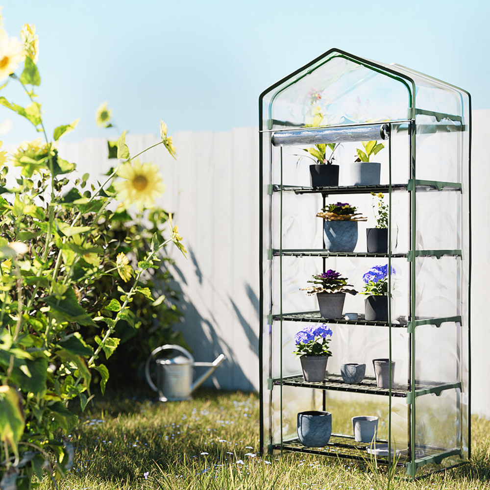 "A compact, multi-tiered greenhouse standing in a sunlit garden, surrounded by plants, designed for small space gardening."